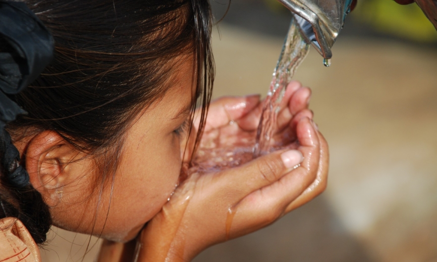 A child drinking water from tap with her hands.