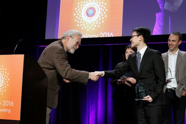 Anthony Leung on a stage holding an award sculpture, shaking hands with the ASCB president