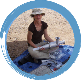 Smiling woman sitting on ground holding a piece of air monitoring equipment