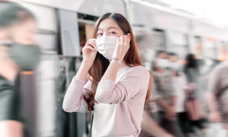 A woman in a crowd of travelers putting on a face mask before boarding a train