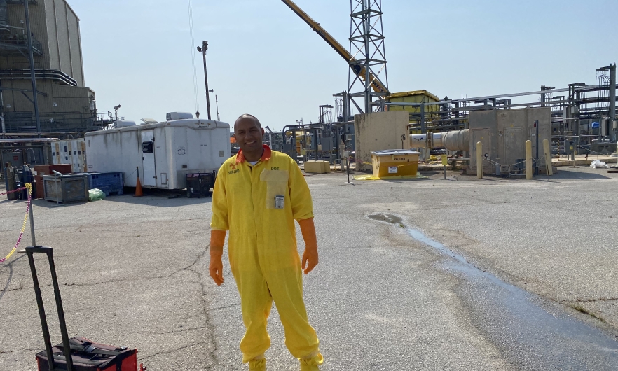 Man standing on an industrial site wearing a bright yellow hazardous material suit