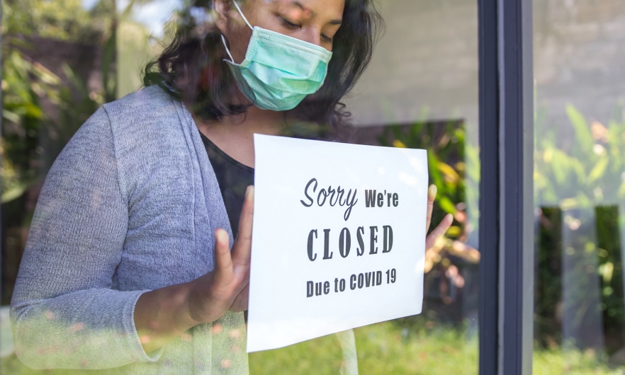 A woman hangs a sign that says "sorry we're closed due to COVID-19" on a storefront window