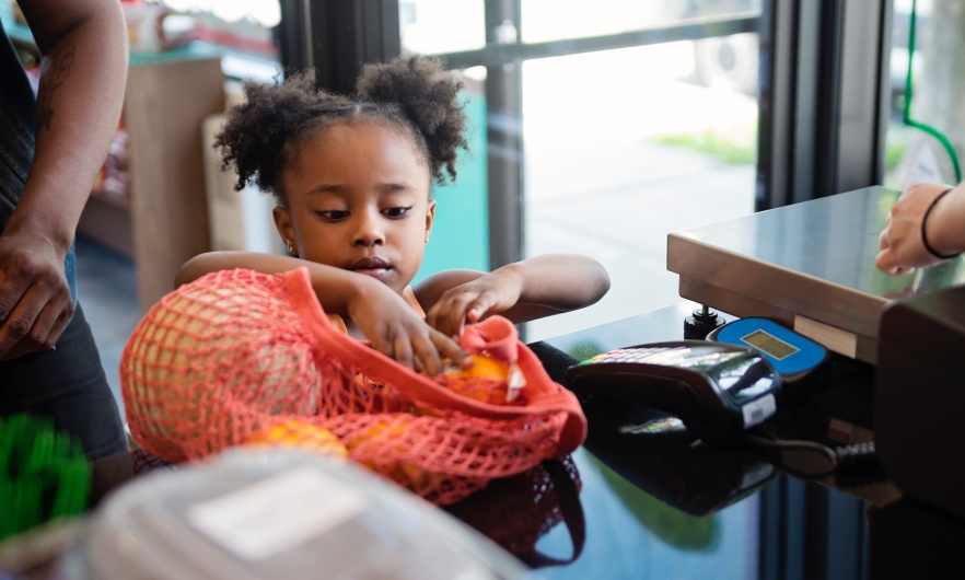 A young girl puts fresh produce in a bag on a store counter