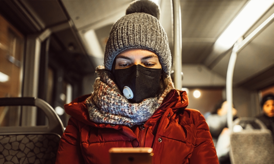 A young woman wearing a face mask and winter clothes uses her smartphone while riding a bus. Getty Images.