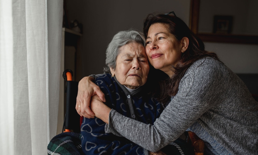caregiver/daughter hugging elderly parent in wheelchair