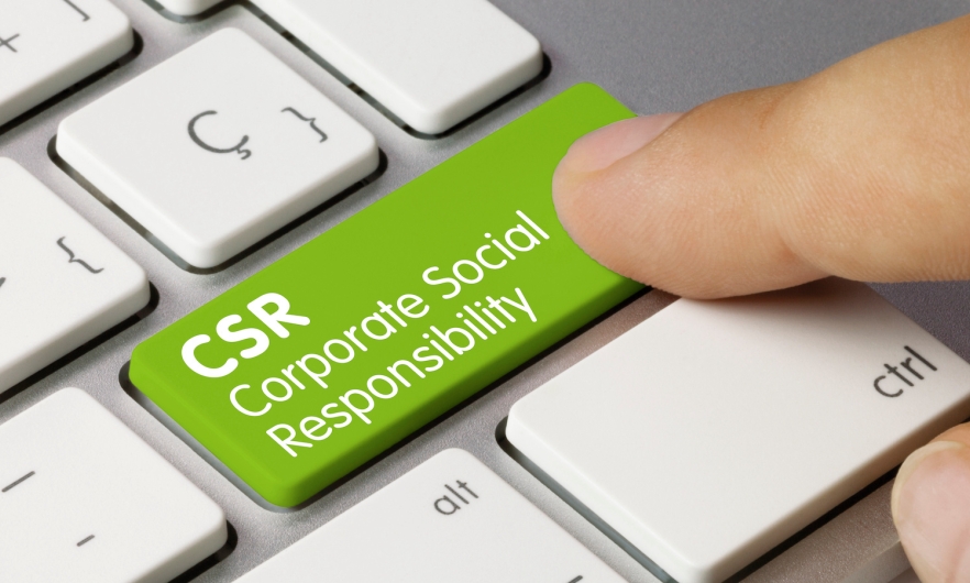 Person's index finger touching a white and silver computer keyboard with a green-colored button labeled "Corporate Social Responsibility" and the abbreviation "CSR"