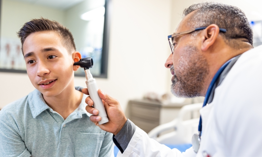 Doctor inspects adolescent boy's ear using otoscope