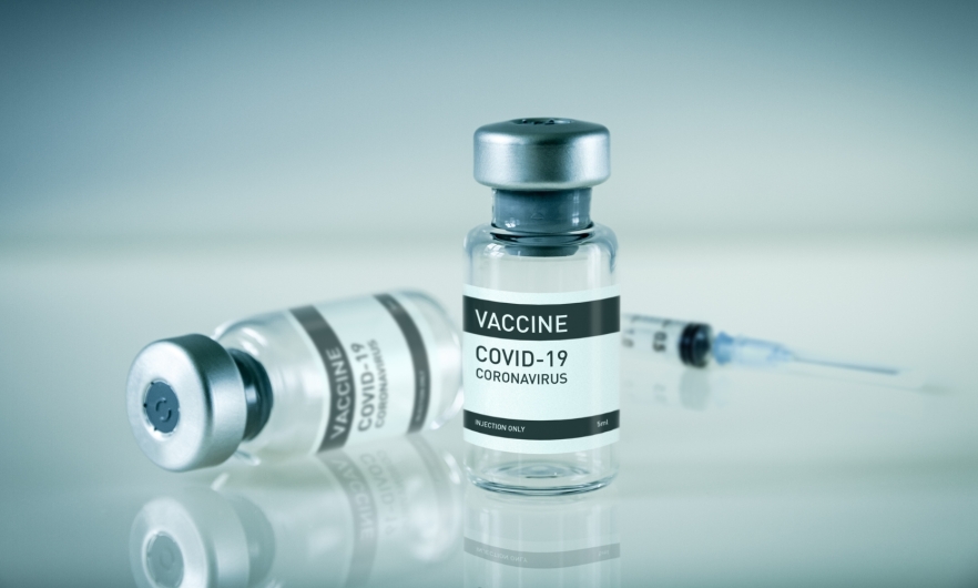 Two vials of the COVID-19 Vaccine with a syringe in the backgroud