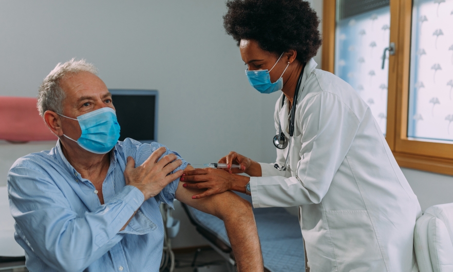 Black female doctor vaccinating elder male