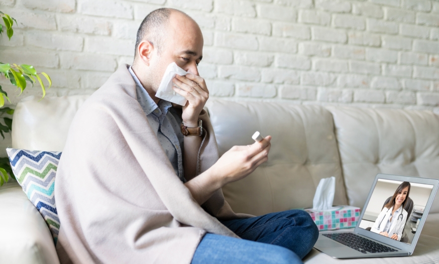 Person sick on their couch looks at home COVID test results during a telehealth appointment