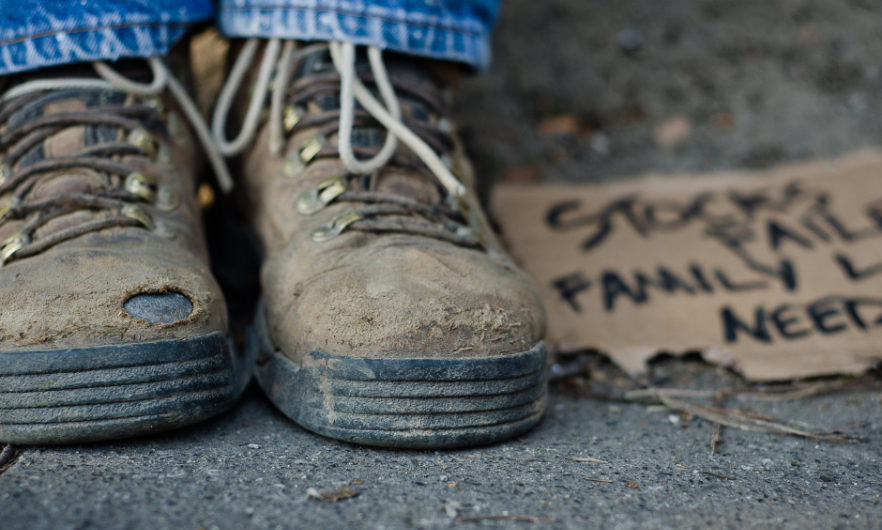 Worn out shoes next to a cardboard sign