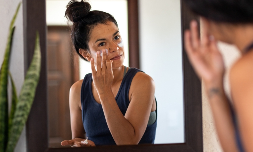 Person applies sunscreen to face in mirror