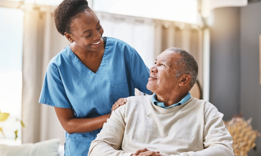 Black health care worker smiling at seated elderly Black man 