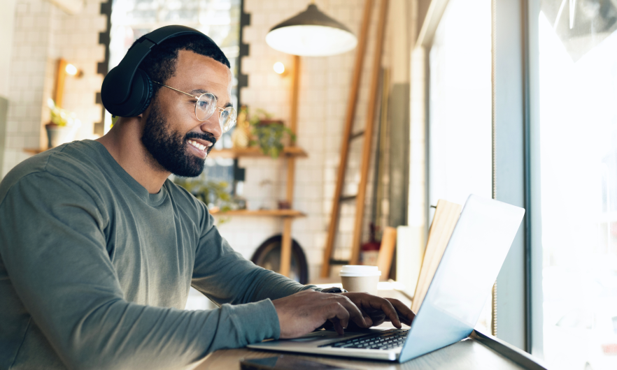 Man wearing headphones and smiling while working on laptop