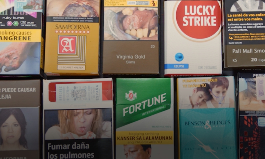 Cigarette packs from around the world lying on a grey table.