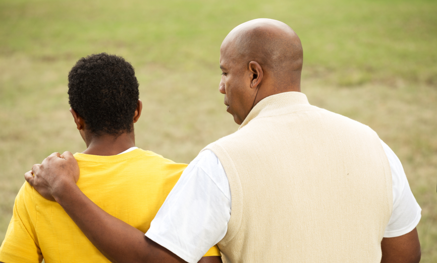 An adult man talking to a teenage boy with his arm around him