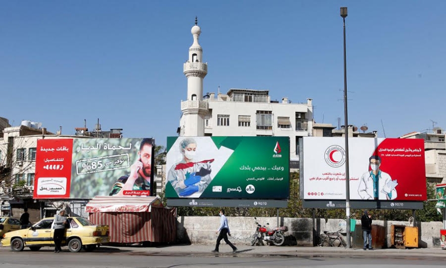 A Syrian man wearing a face mask walks in front of COVID-19 posters, Damascus. April 1, 2020.