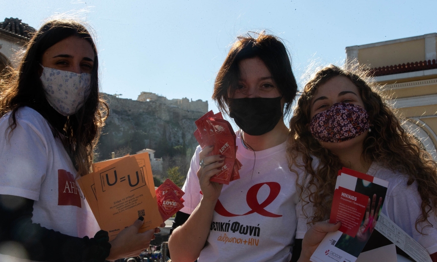Three female volunteers, wearing cloth face masks, pose with leaflets about sexual health in Athens, Greece, on World AIDS Day, Dec. 1, 2021.
