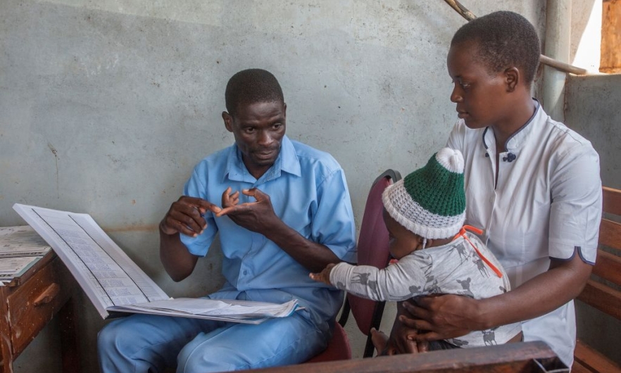 A health surveillance assistant talks to a mother at a malaria vaccine screening table in Lilongwe, Malawi, April 23, 2019.