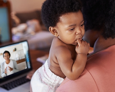 Woman holding a child while working on a computer