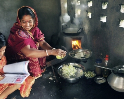 Woman in Dhaka uses a cookstove while a child next to her reads