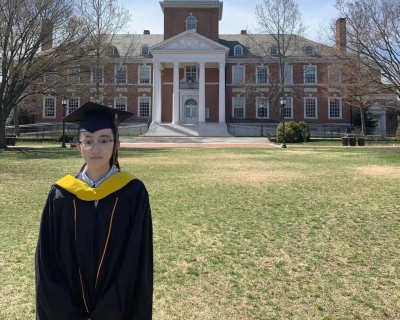 Young woman in cap and gown in front of a university building
