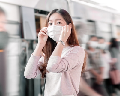 A woman in a crowd of travelers putting on a face mask before boarding a train
