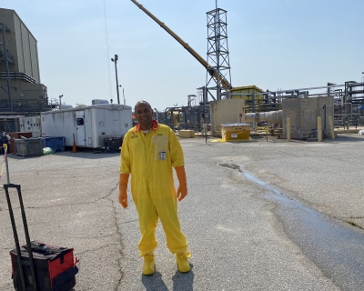Man standing on an industrial site wearing a bright yellow hazardous material suit
