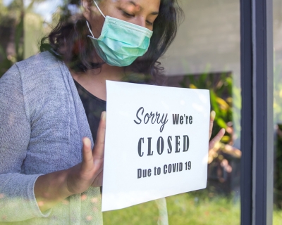 A woman hangs a sign that says "sorry we're closed due to COVID-19" on a storefront window