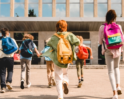 Children running toward school with backpacks on