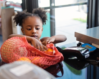A young girl puts fresh produce in a bag on a store counter
