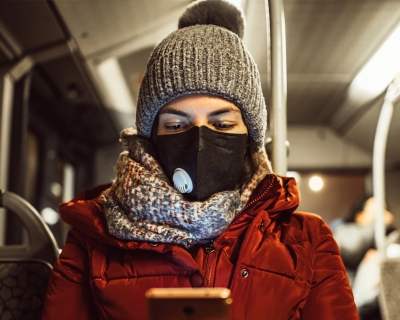 A young woman wearing a face mask and winter clothes uses her smartphone while riding a bus. Getty Images.