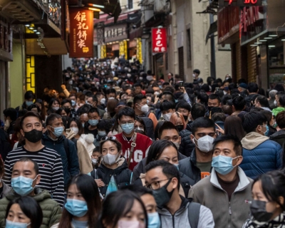 Large crowd of people wearing masks walking a narrow street in china 
