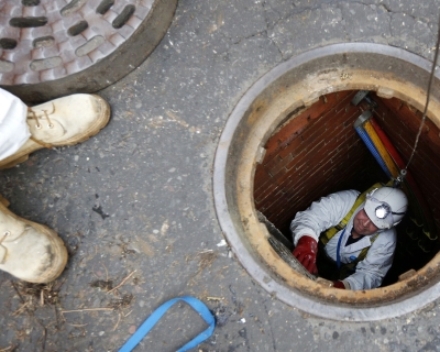 Open sewer in the middle of the street with worker climbing up while another supervises