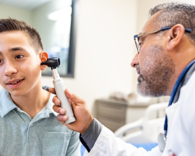 Doctor inspects adolescent boy's ear using otoscope
