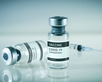 Two vials of the COVID-19 Vaccine with a syringe in the backgroud