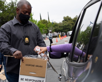 A person in their car emptying prescription bottles into a box held by a member of the DEA