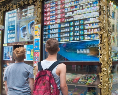 Two young boys stand outside a tobacco vendor in Switzerland, observing a massive display of cigarette products and advertising visible at children's eye level to passersby outside