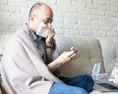 Person sick on their couch looks at home COVID test results during a telehealth appointment