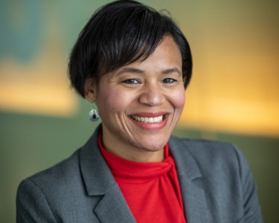 A headshot of department chair Keshia Pollack Porter. She smiles at the camera while wearing a red blouse under her grey suit jacket.
