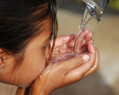 A child drinking water from tap with her hands.