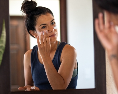 Person applies sunscreen to face in mirror