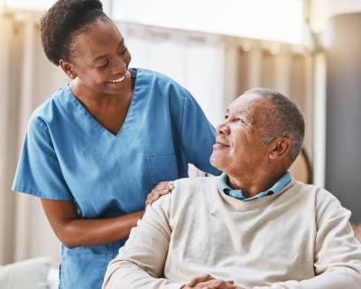Black health care worker smiling at seated elderly Black man 