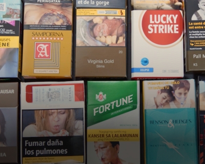 Cigarette packs from around the world lying on a grey table.