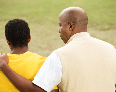 An adult man talking to a teenage boy with his arm around him