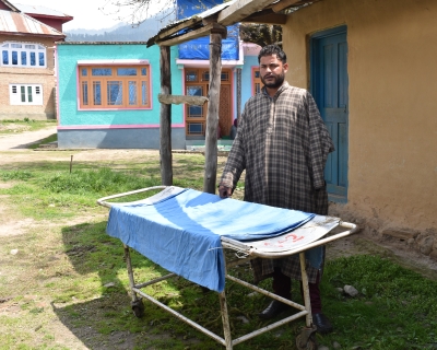 Zahoor Ahmed Bhat stands outside his house in the Anantnag district of South Kashmir with the stretcher that his wife, Shakeela AkhterAkhter died on before she could get to an emergency maternal health care center. Image by Aliya Bashir.