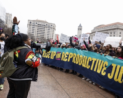 A woman speaks into a microphone, addressing a crowd behind a banner reading &quot;Rise up for Reproductive Justice&quot; at a January 22 protest in Washington, DC. 