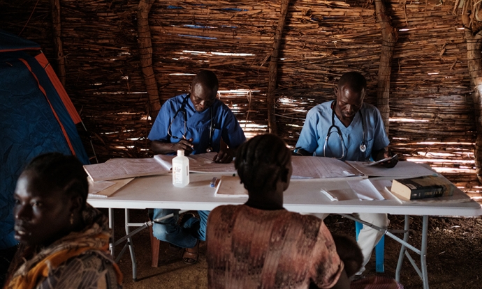 Two doctors sitting at a table consult with patients  in a clinic a camp for internally displaced persons.