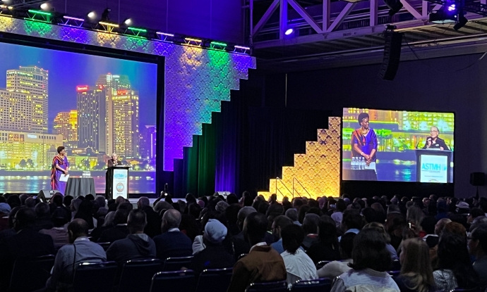 Monique Wasunna stands on a stage delivering her keynote to a packed audience. 