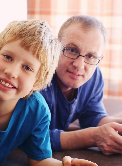 Preteen boy and man smile while looking at electronic device together